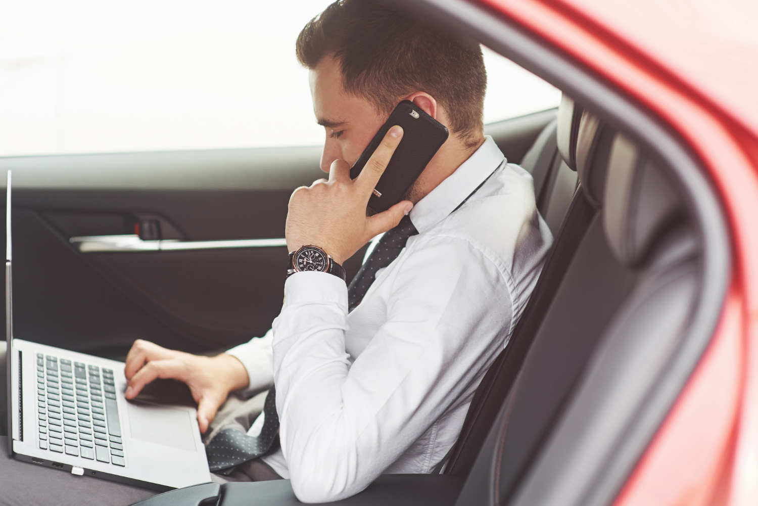 person using mobile and laptop in a car